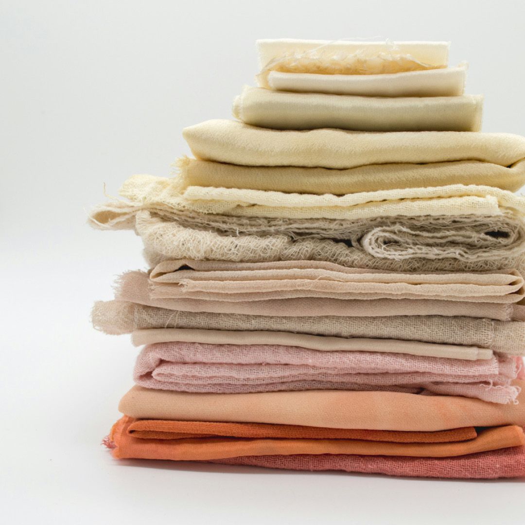 A neatly folded stack of varying fabrics all in different natural dye colors from orange to neutral to soft yellow.