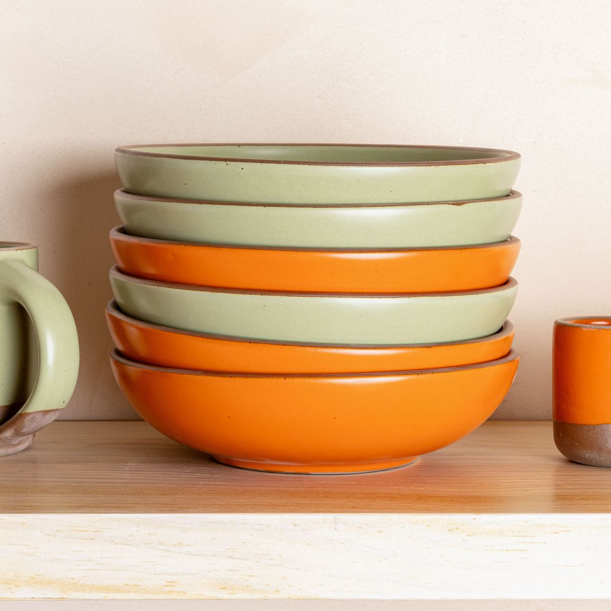 A stack of shallow dinner bowls in calming sage green and bold orange colors.