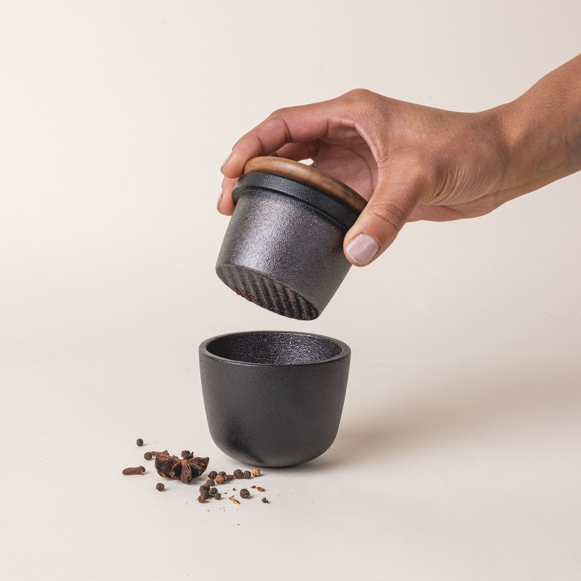 A short round cast iron jar with a topper grinder and wooden lid. Ground seasoning is next to it.