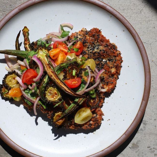 An artful colorful entree is plated on a ceramic plate in a white color.