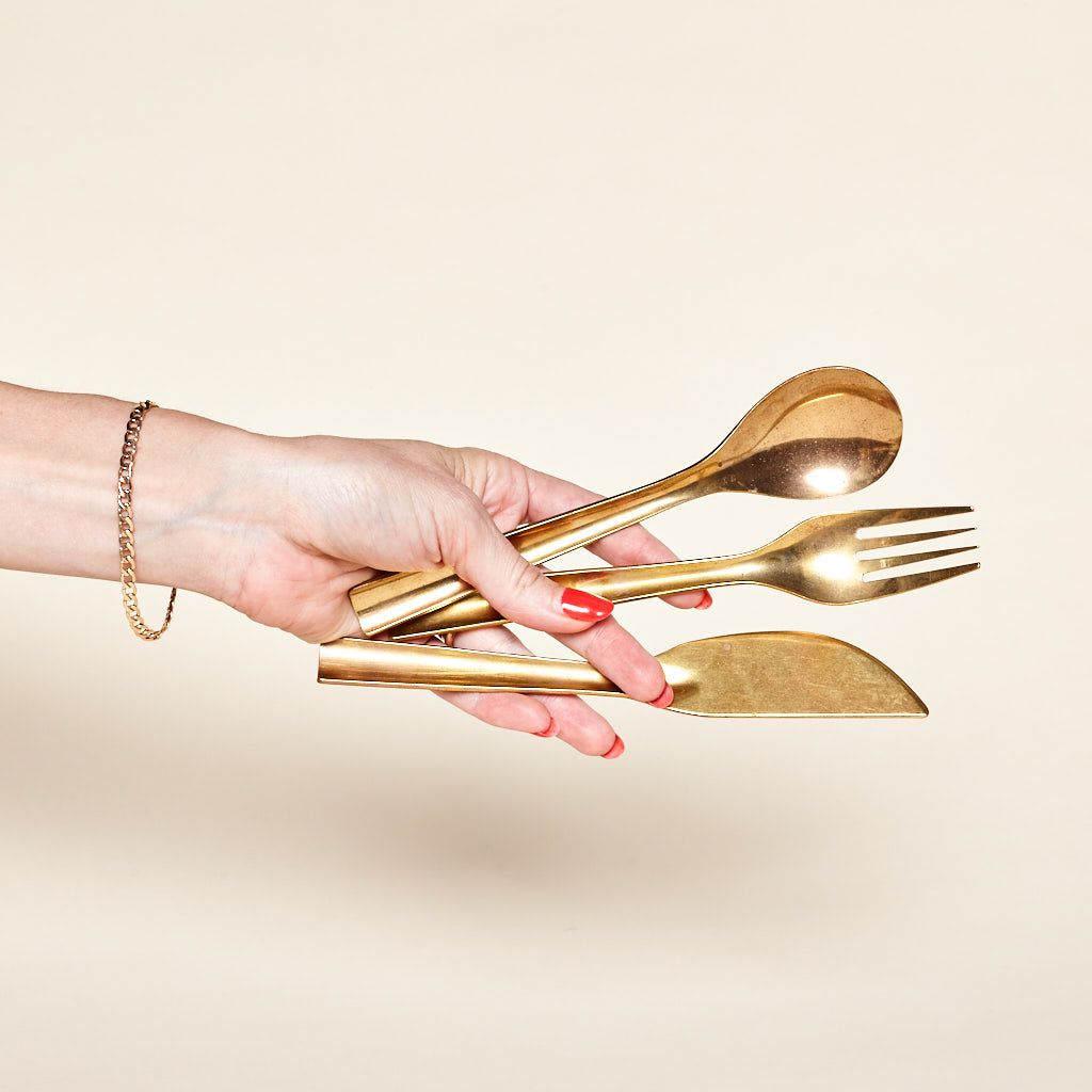 A hand holds a brass spoon, fork and knife