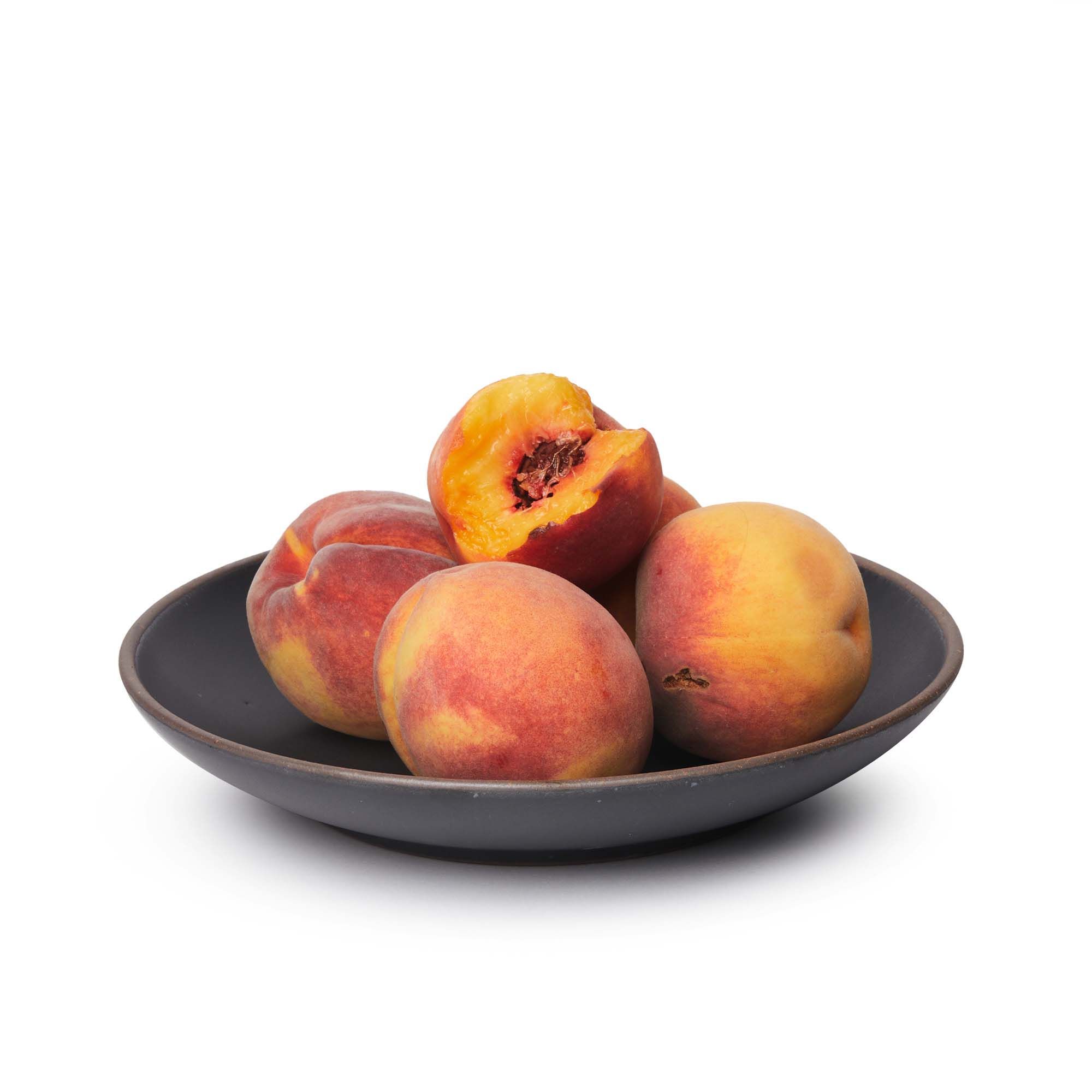Peaches in a large ceramic plate with a curved bowl edge in a graphite black color featuring iron speckles and an unglazed rim.
