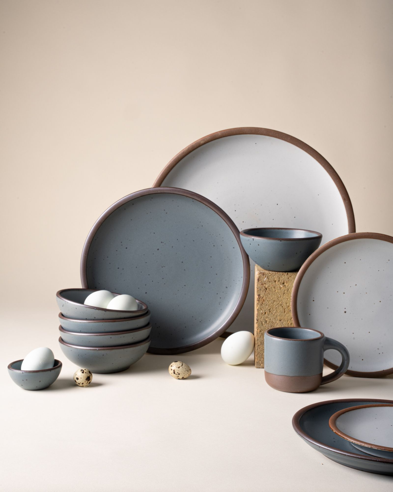 Ceramic plates and bowls in various sizes and a small mug in blue-grey and cool white colors, artfully arranged with eggs.