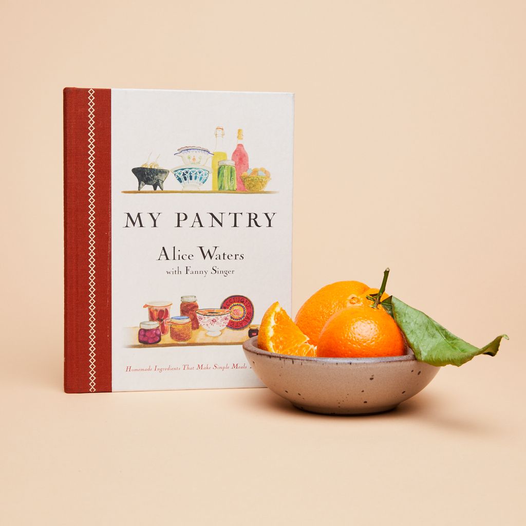 A bowl of oranges next to a copy of Alice Waters's cookbook called My Pantry