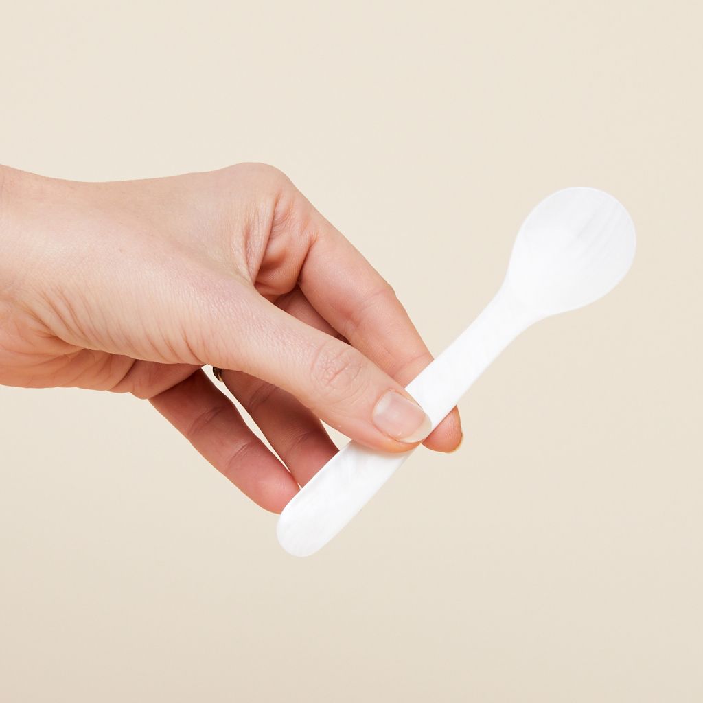 A hand holds a white spoon that is made of shell
