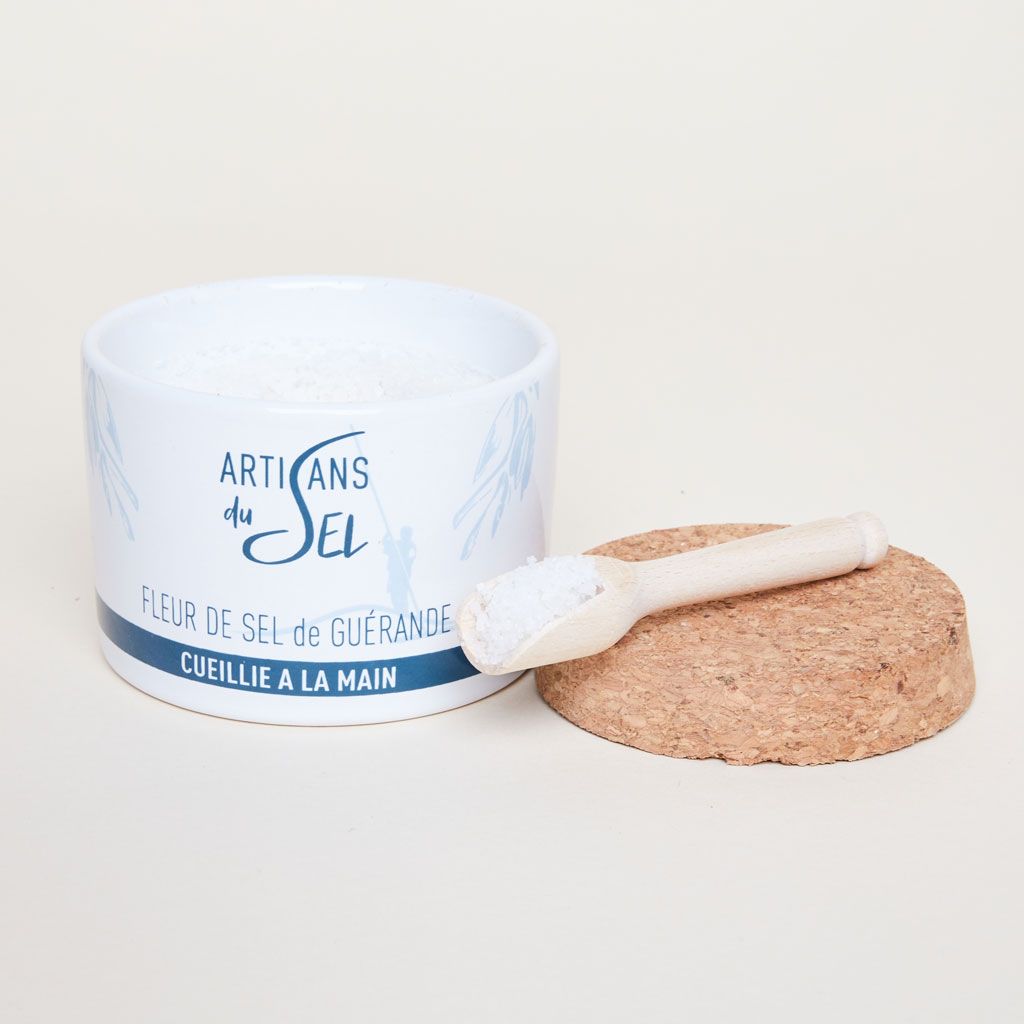 A white and blue container for fleur de sel with its cork top removed, revealing the salt inside and wooden spoon