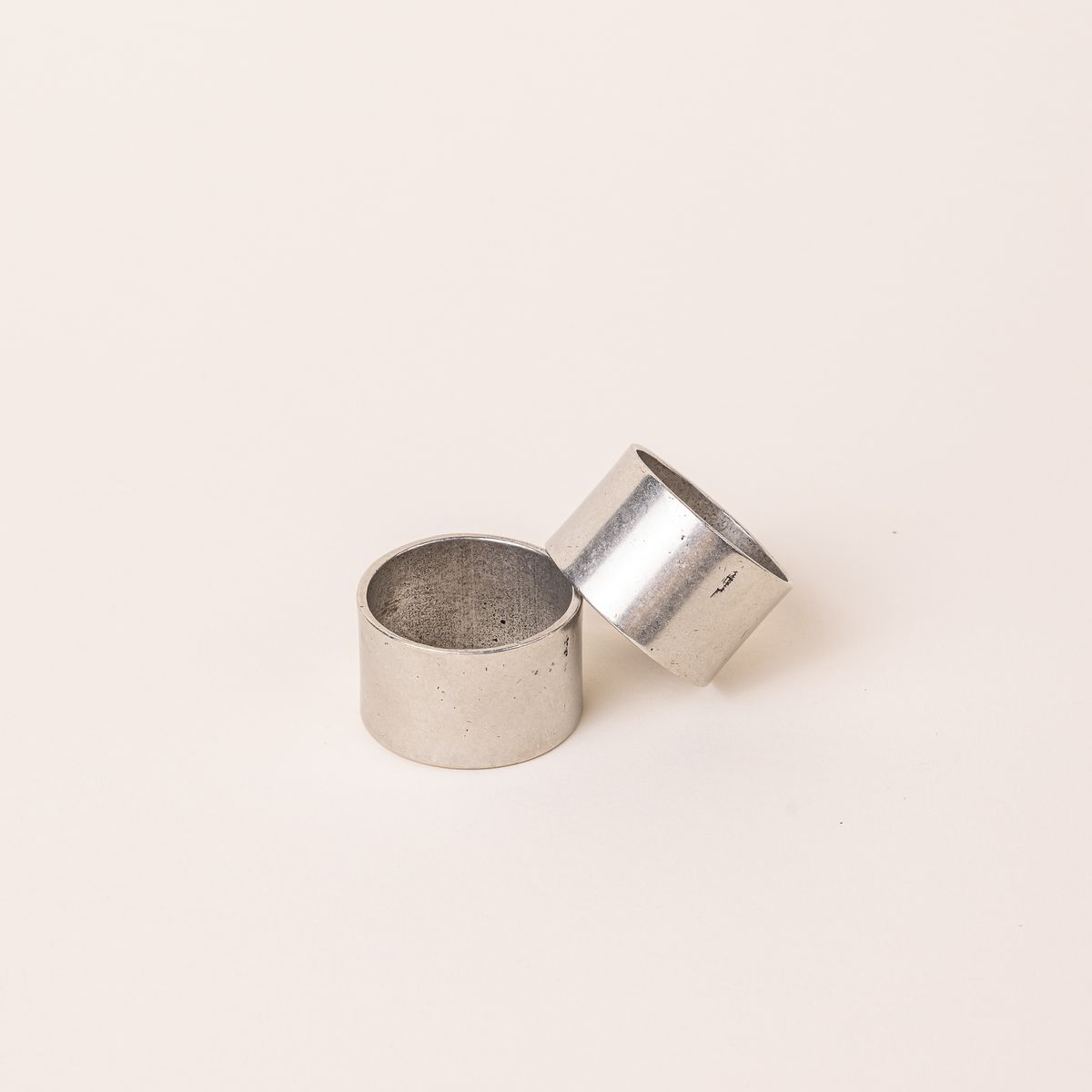 Two simple silver pewter napkin rings - one is leaning on the other.