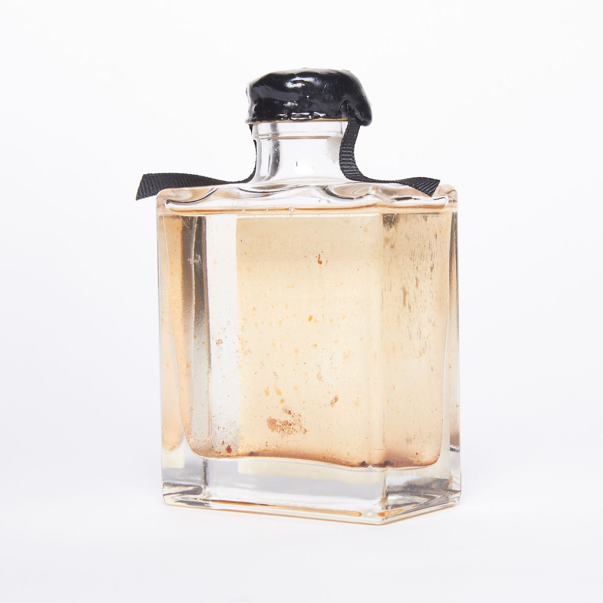Backside of a clear bottle full of yellowish cloudy liquid with black wax covering the top