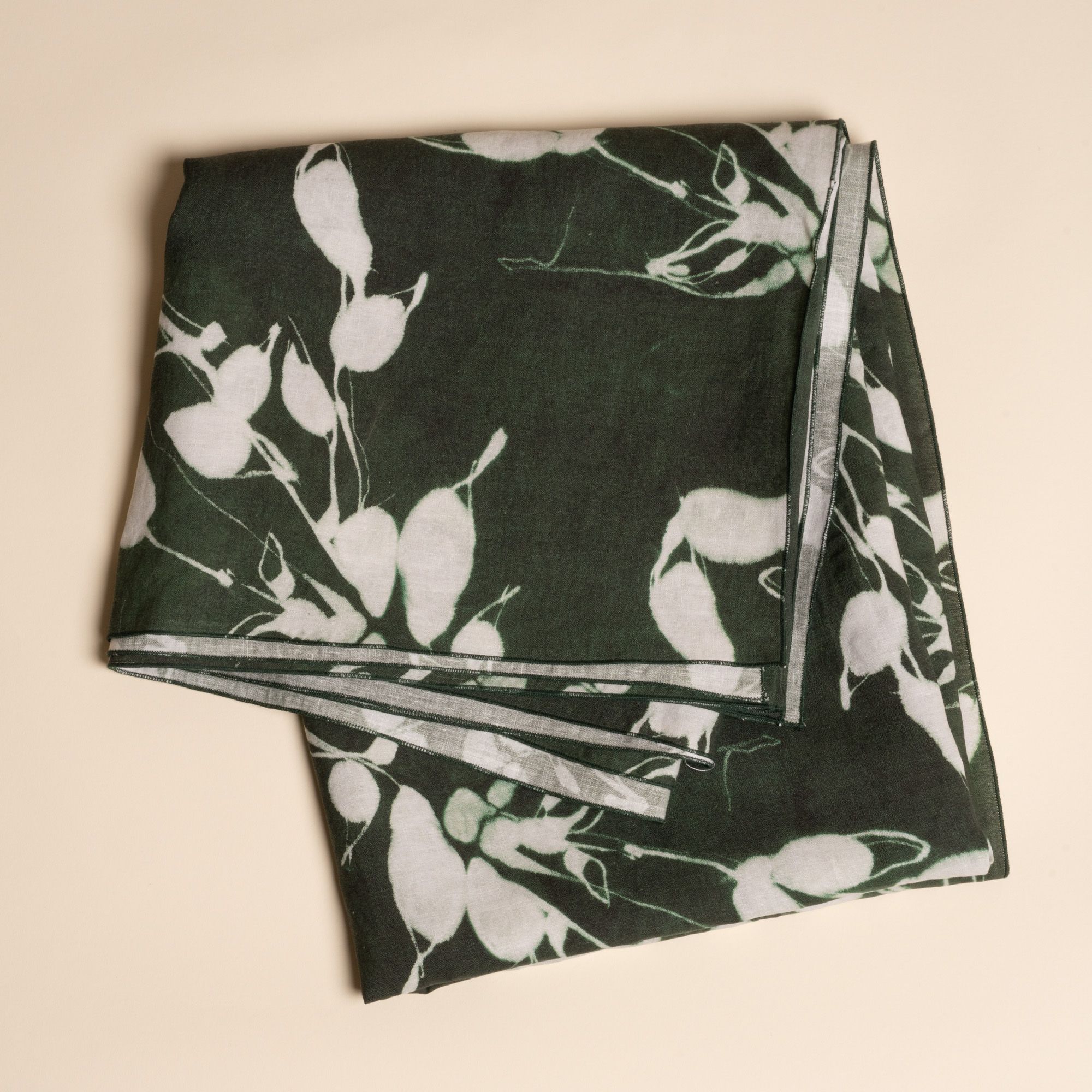 A folded tablecloth in a dark green color with white botanical print on a neutral background.