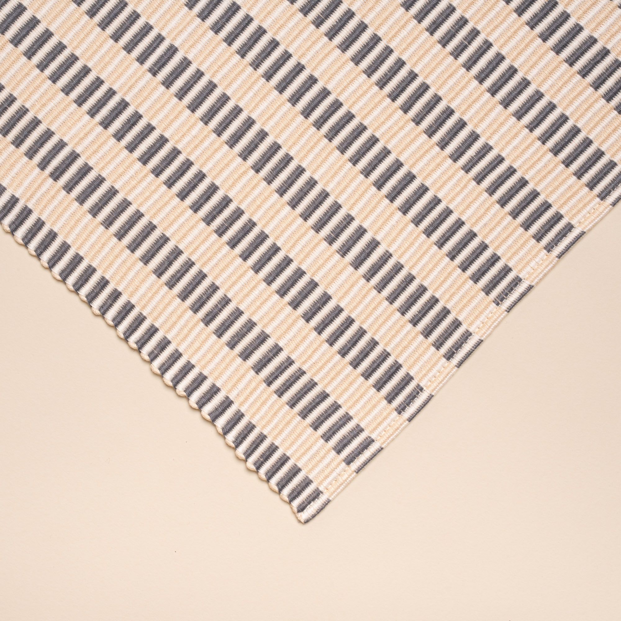 A closeup of a corner of a woven placemat with thin horizontal striped grey and natural colors