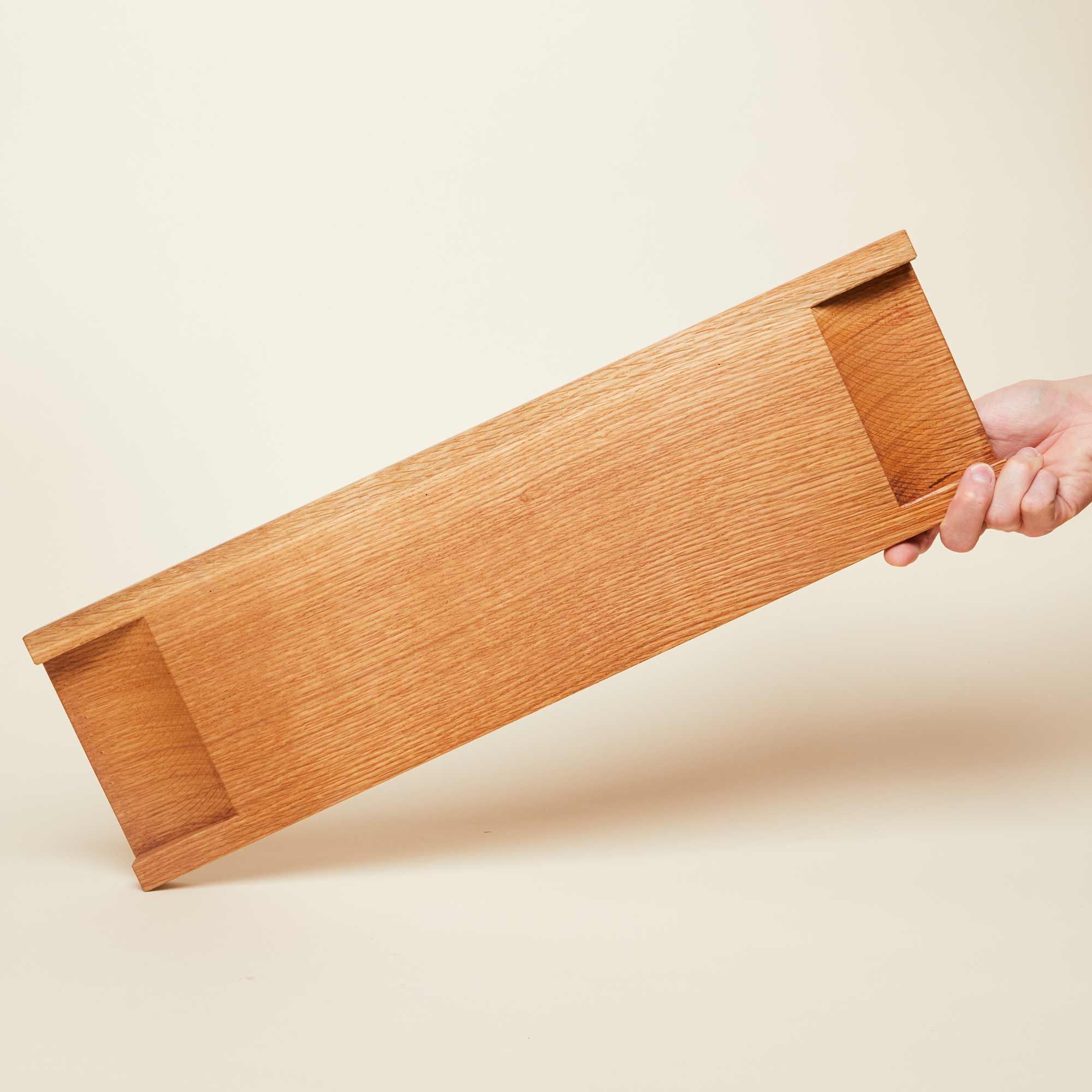 Underside of charcuterie board with handles and a hand holding the board at an angle
