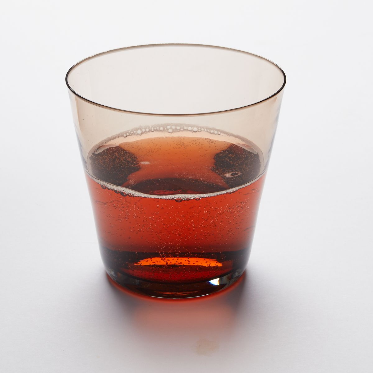 A short drinking glass made of walnut colored glass, filled with amber drink