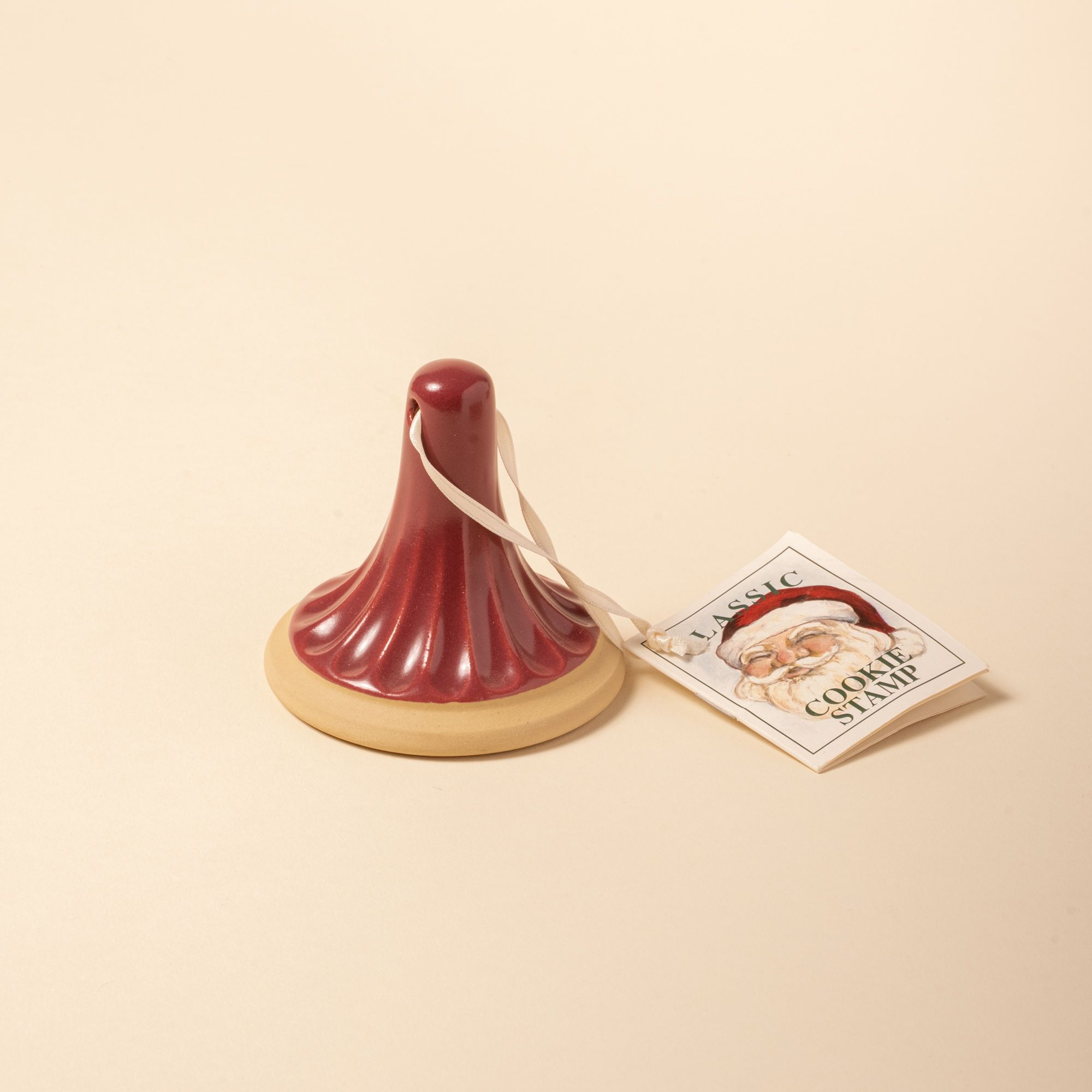 A red-handled ceramic cookie stamp with a fluted design, attached to a tag labeled “Classic Cookie Stamp” featuring Santa Claus.
