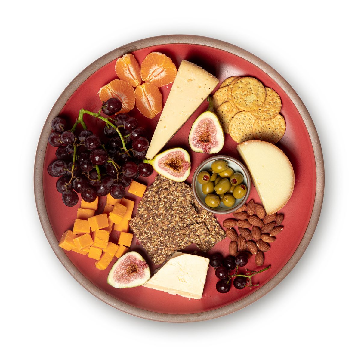 Charcuterie on a large ceramic platter in a bold red color featuring iron speckles and an unglazed rim