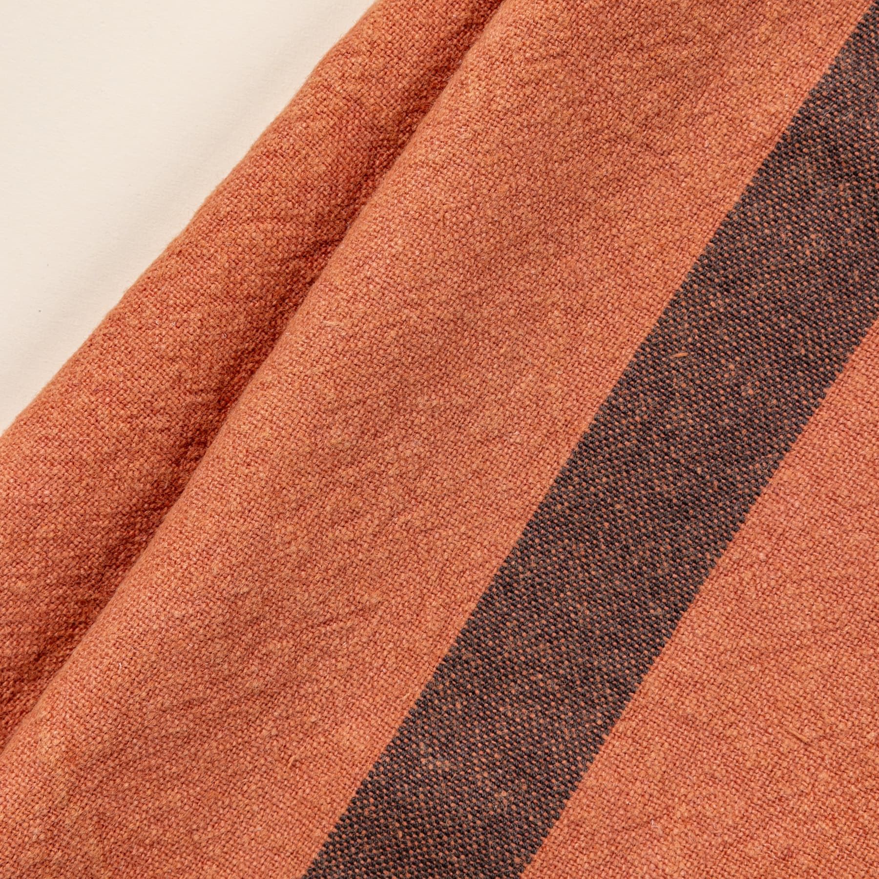 A close up of a folded linen towel in a terracotta color with a plum stripe in the middle