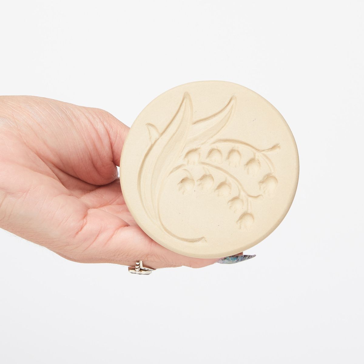 Hand holding a cookie stamp showing the bottom featuring the design of a lily of the valley