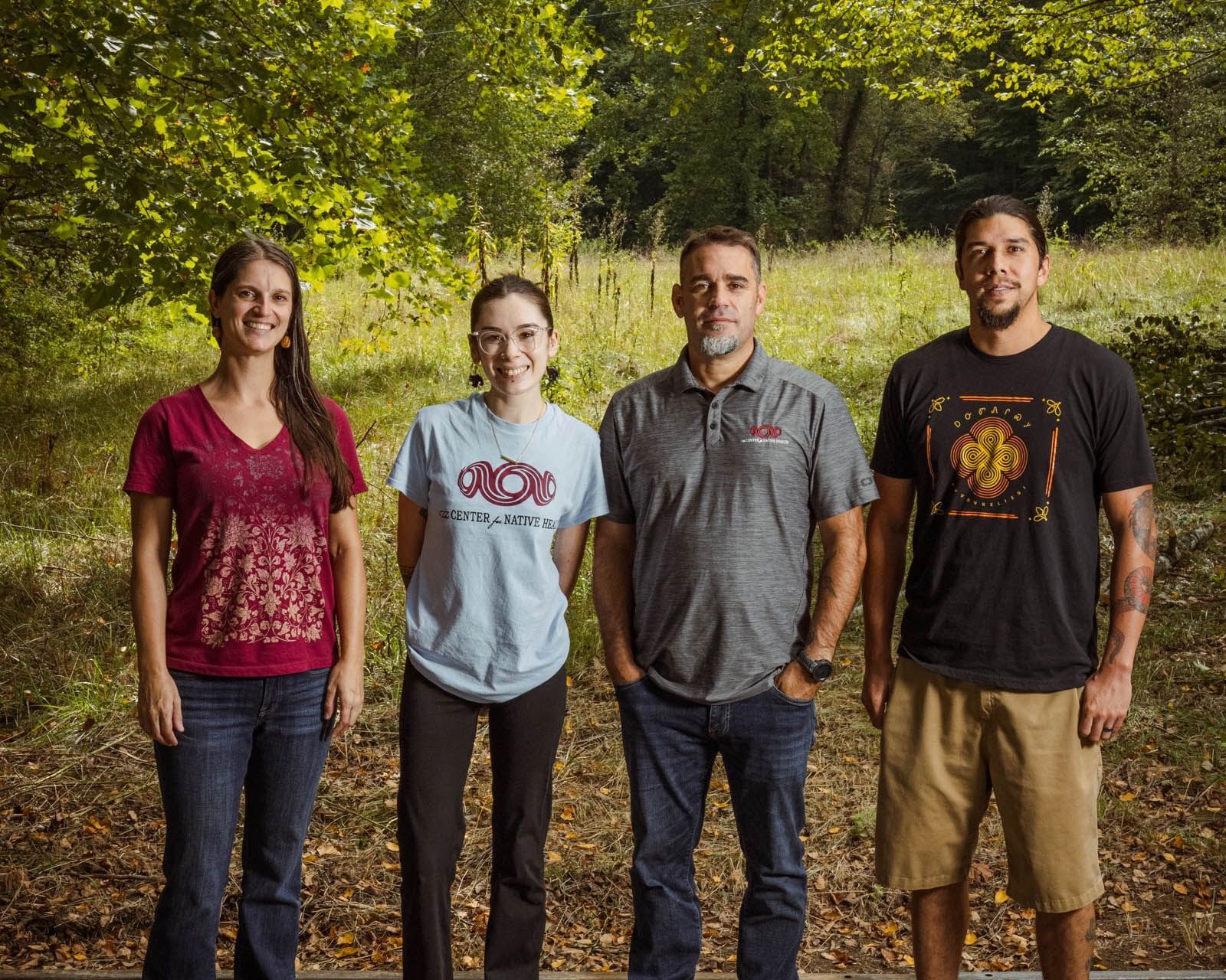 4 people stand outdoors smiling or looking directly at the camera.