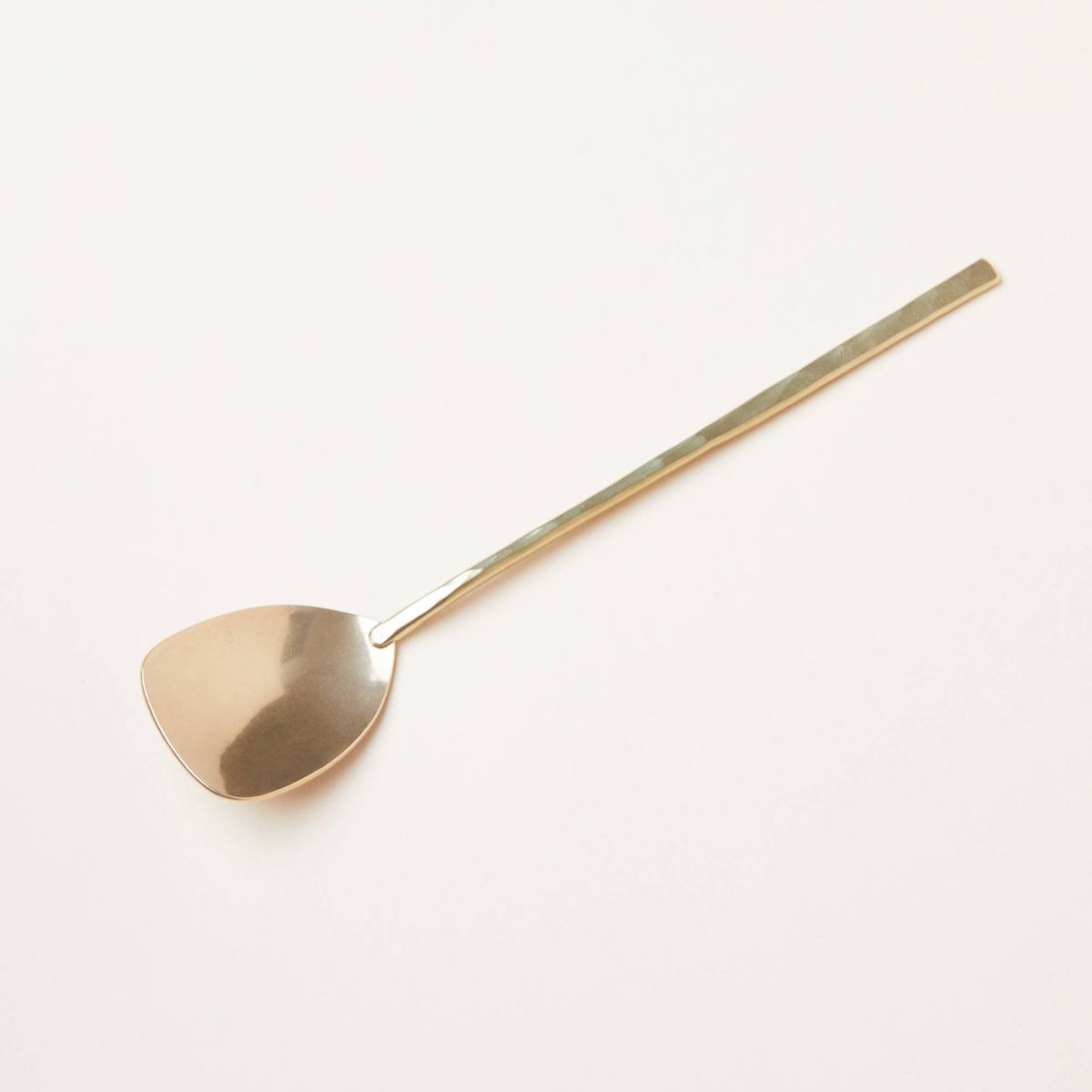 A long-handled brass spoon that is squared-off at the end