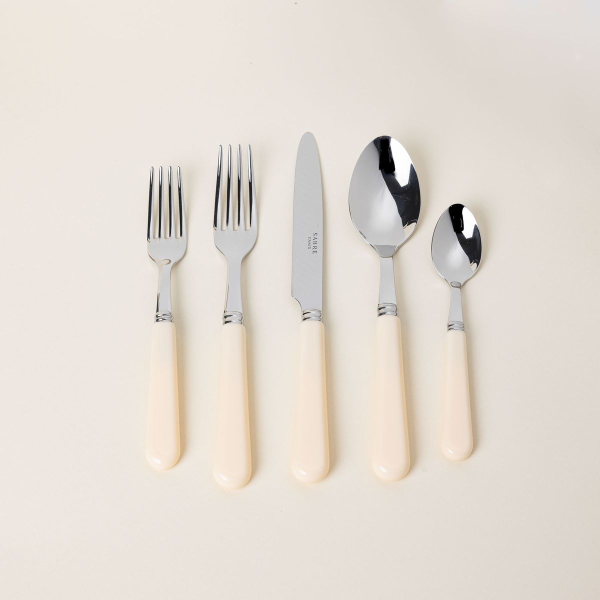 A five piece flatware set with shiny utensils and matte cream handles