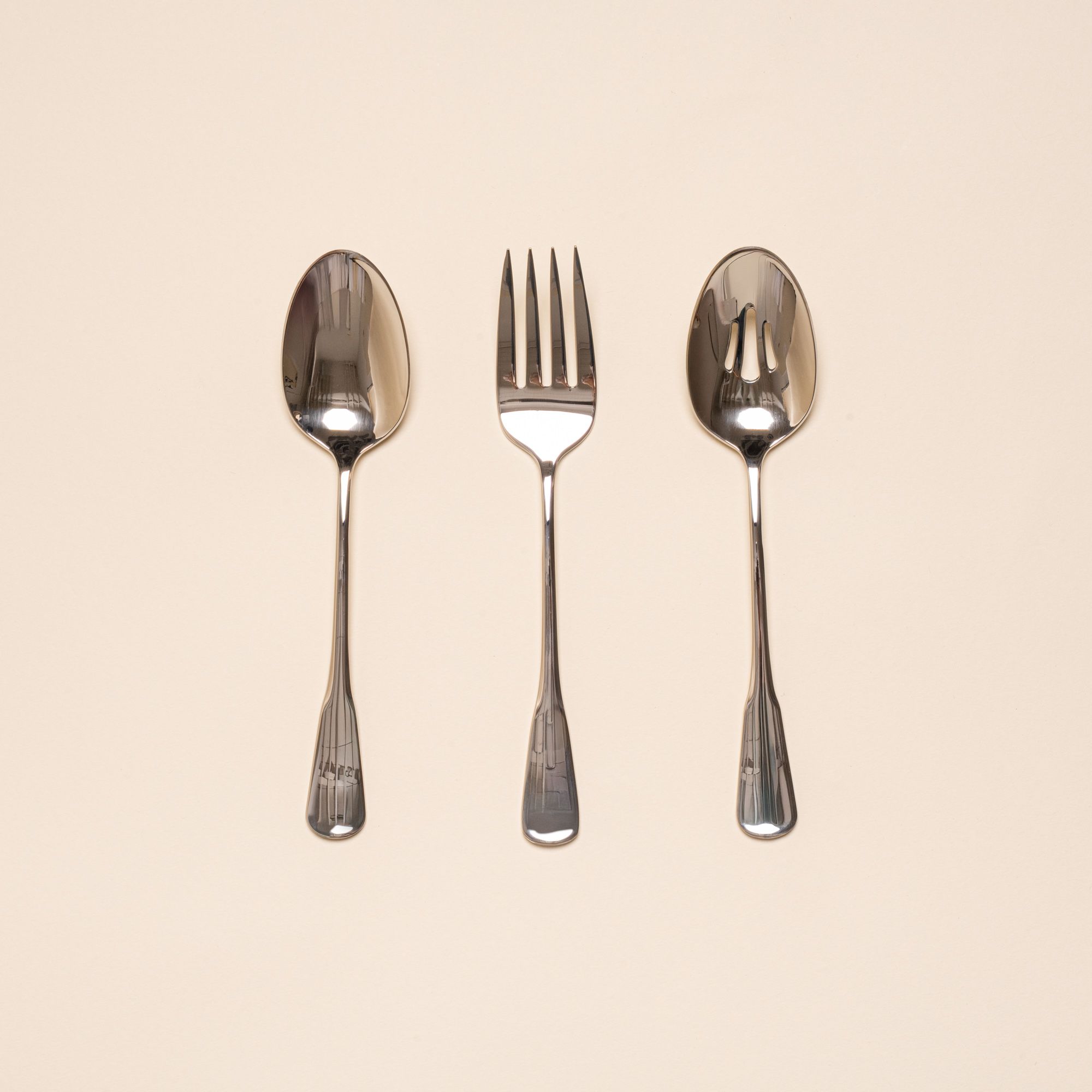 Three stainless steel serving utensils including a serving fork, serving spoon, and pierced spoon in a polished finish with a classic design