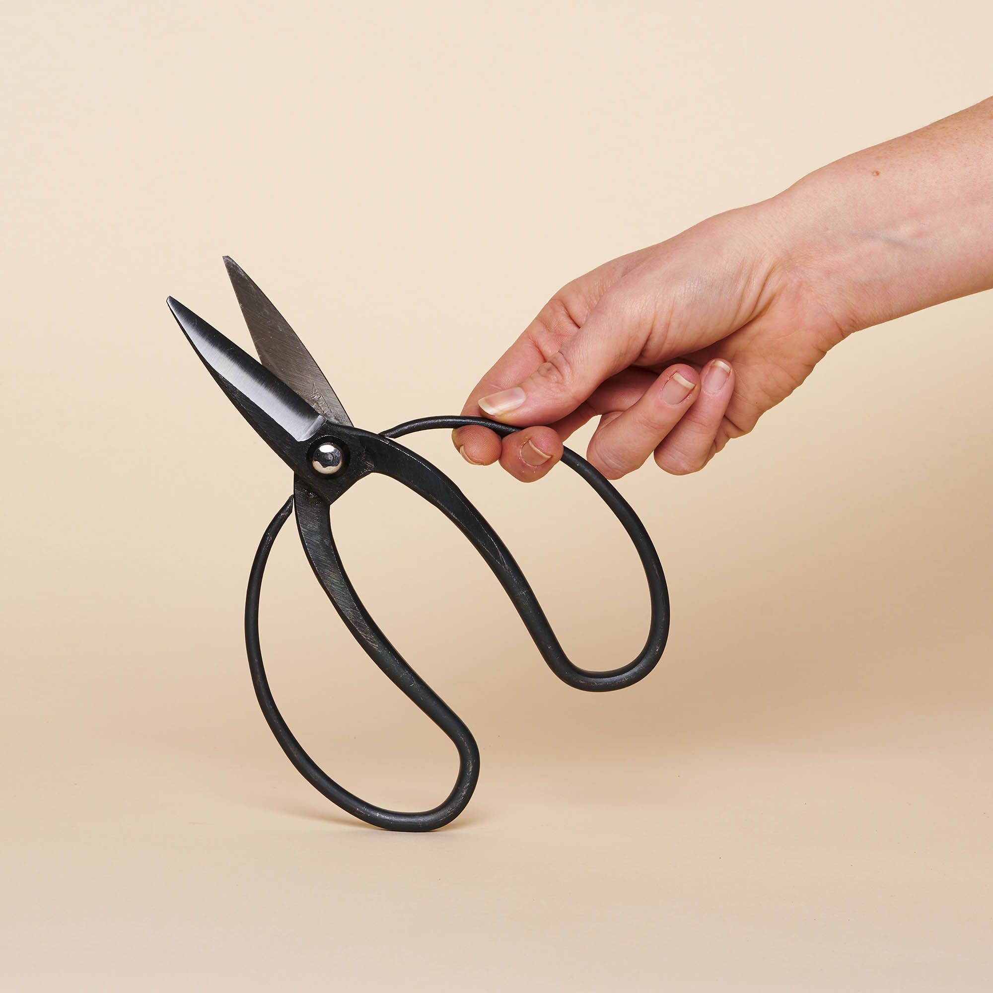 A hand holds an open pair of Japanese Gardening Shears, with a black balloon-shaped handle.