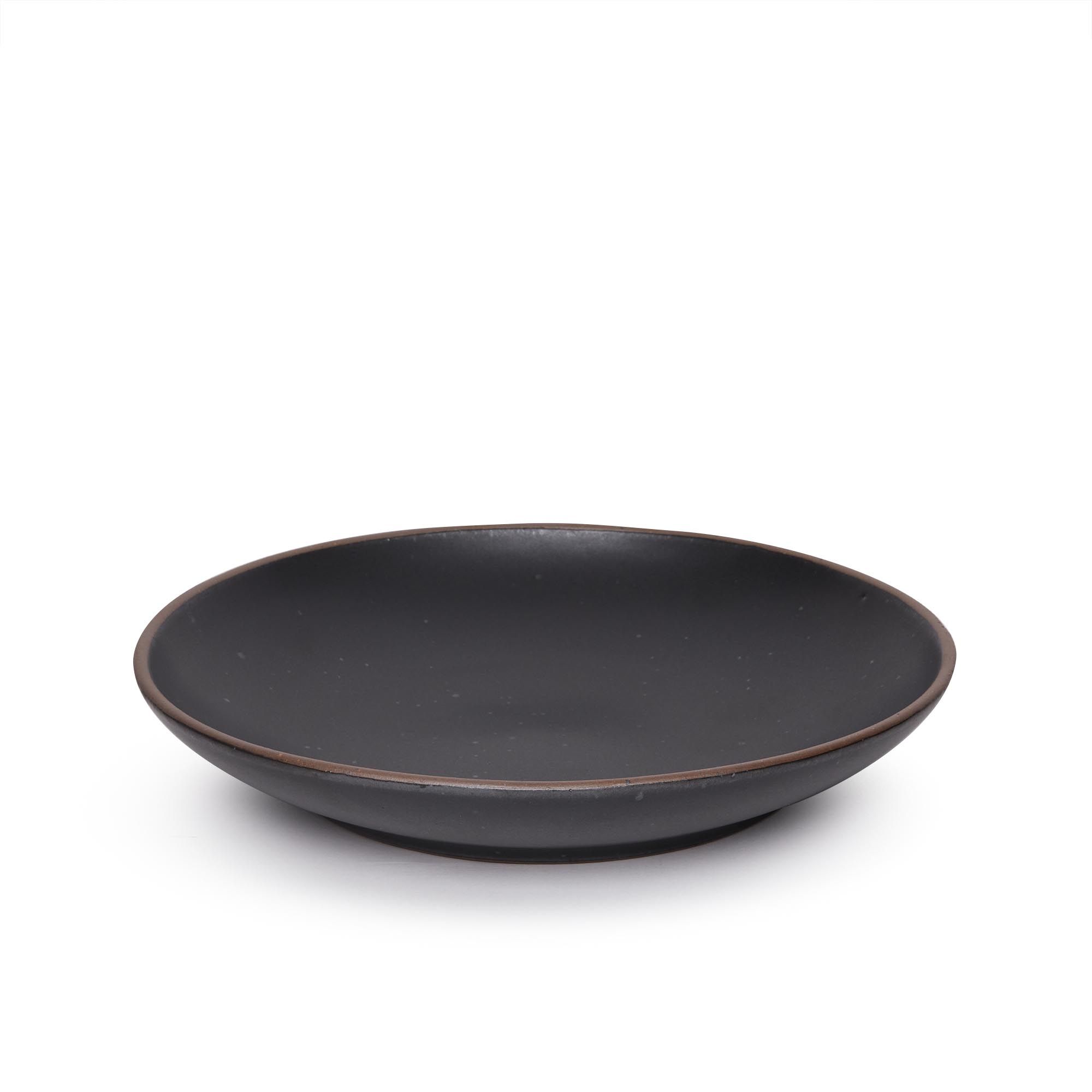 A large ceramic plate with a curved bowl edge in a graphite black color featuring iron speckles and an unglazed rim.