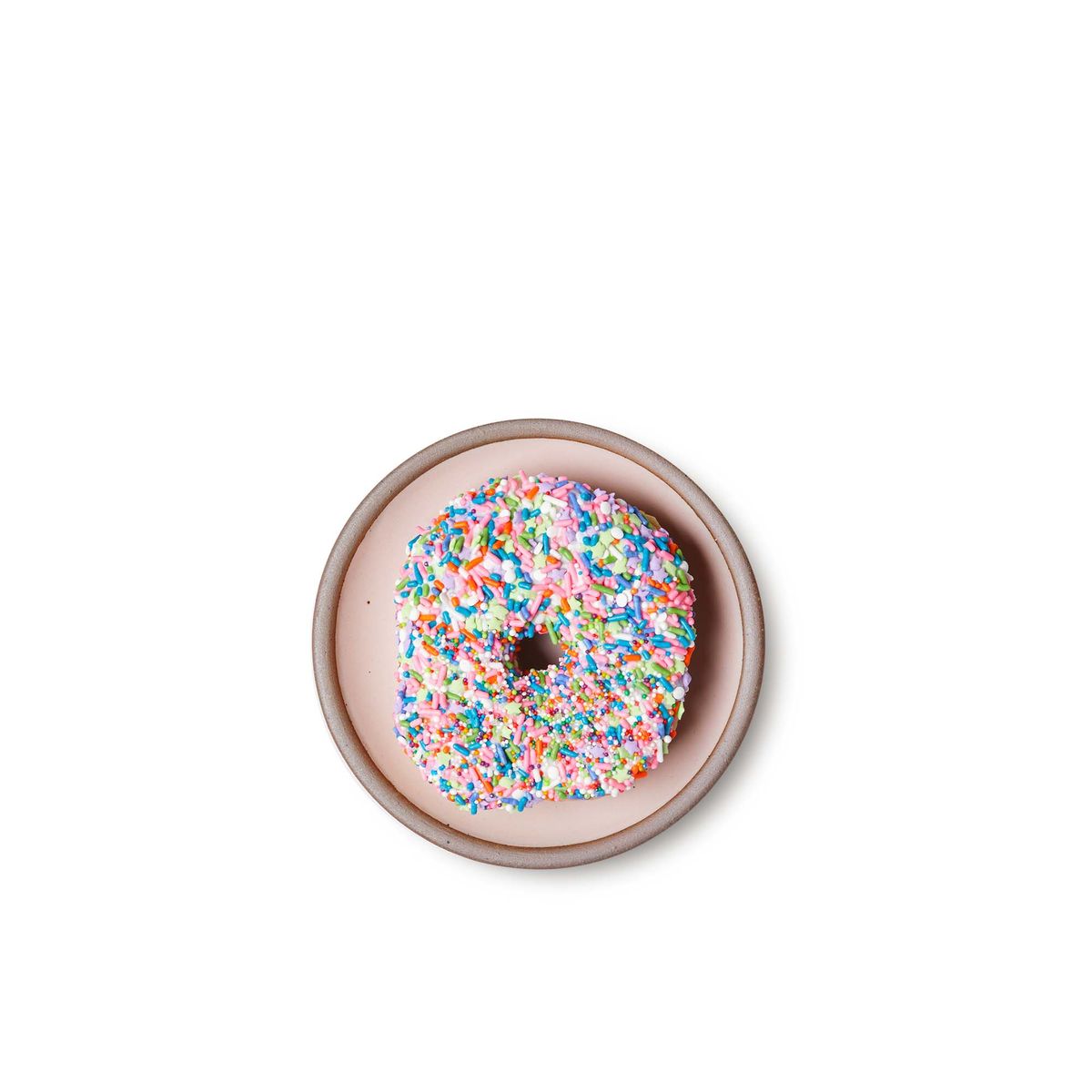 A sprinkled donut on a dessert sized ceramic plate in a soft light pink color featuring iron speckles and an unglazed rim