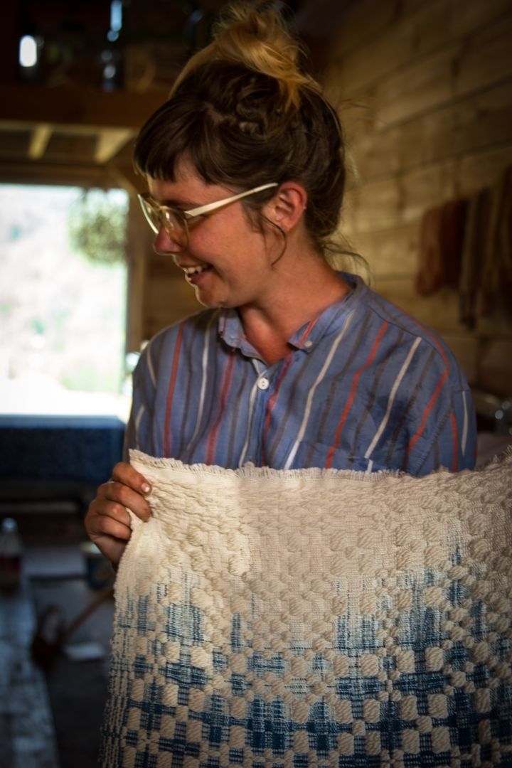 A woman holds a large weaving in white and blue colors