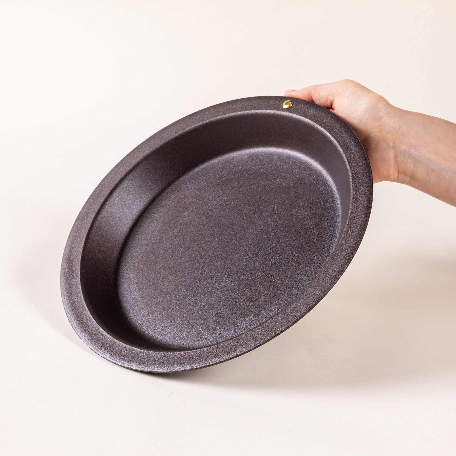 A hand holds a simple iron pie dish with a wide rim and shallow body