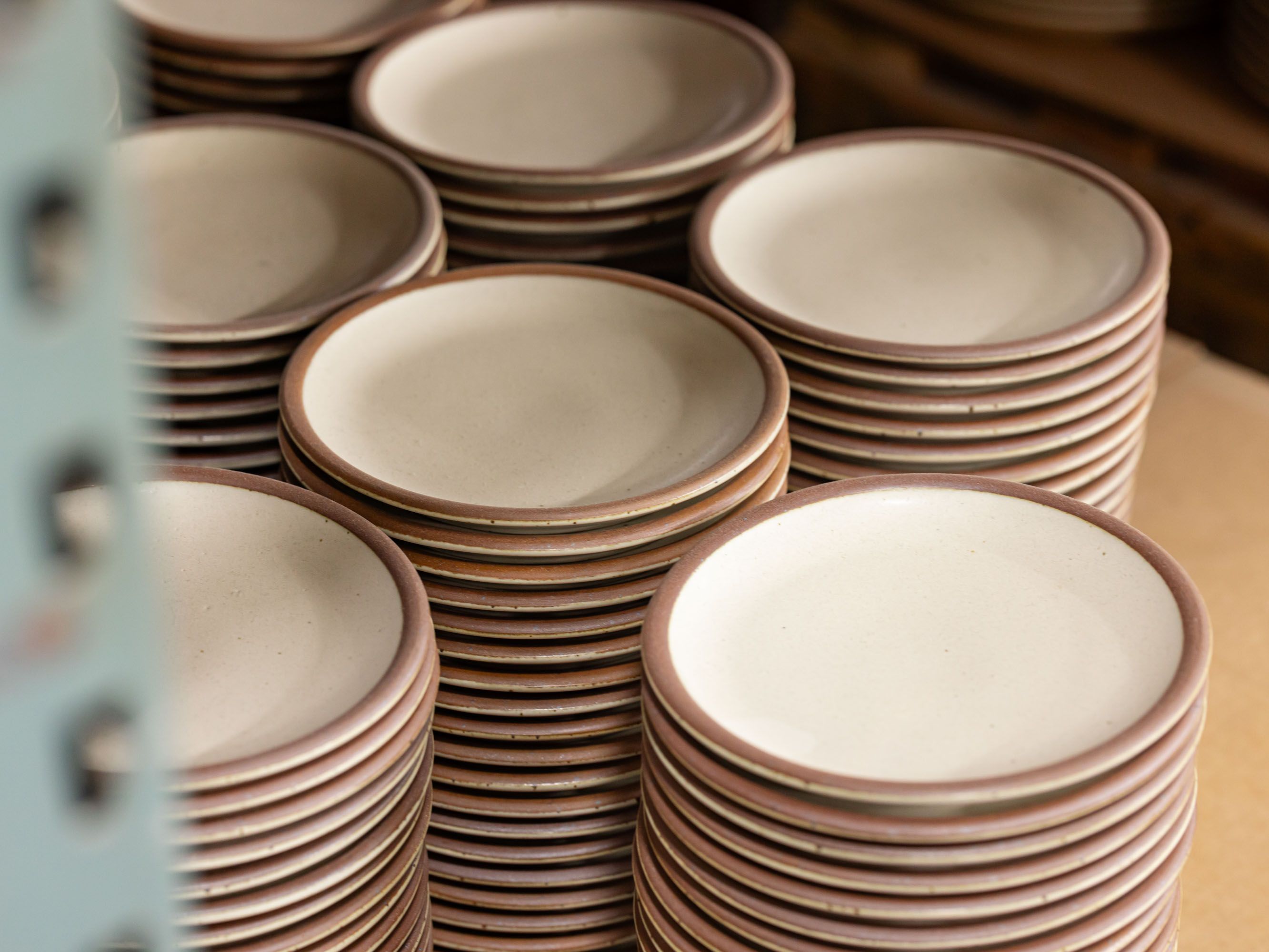 Stacks of off-white, cream colored ceramic plates with unglazed rims.