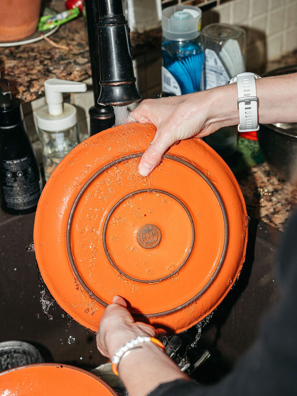 Hands holding a large orange plate under the kitchen faucet to wash off.