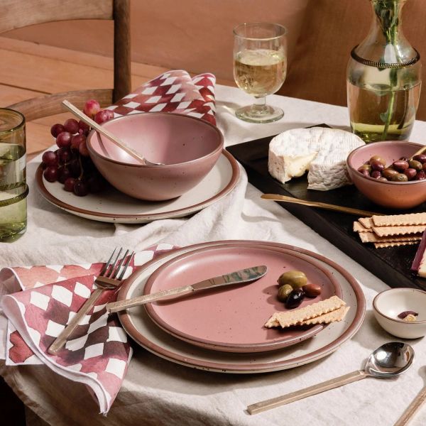 A table setting with ceramic dinnerware in cream and soft pink colors, patterned linens, a cheeseboard and more.
