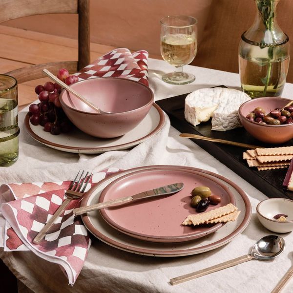 A table setting with ceramic dinnerware in cream and soft pink colors, patterned linens, a cheeseboard and more.