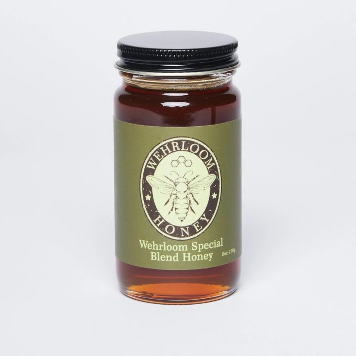 Glass jar filled with golden honey with a black lid and green label that reads 'Wherloom special honey blend'.