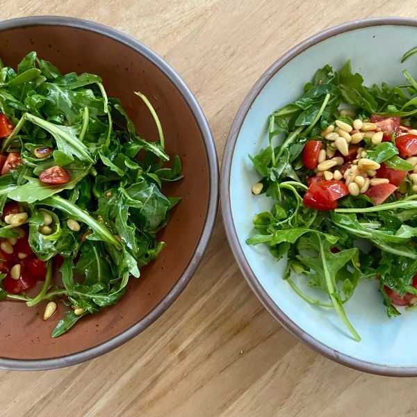 Two ceramic bowls in terracotta and cool white colors with a corn tomato salad in each on a table.