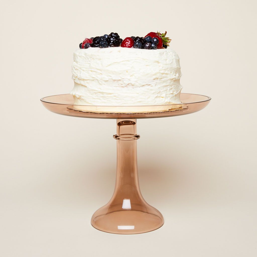 A white cake with berries on top sits on an amber glass cake stand