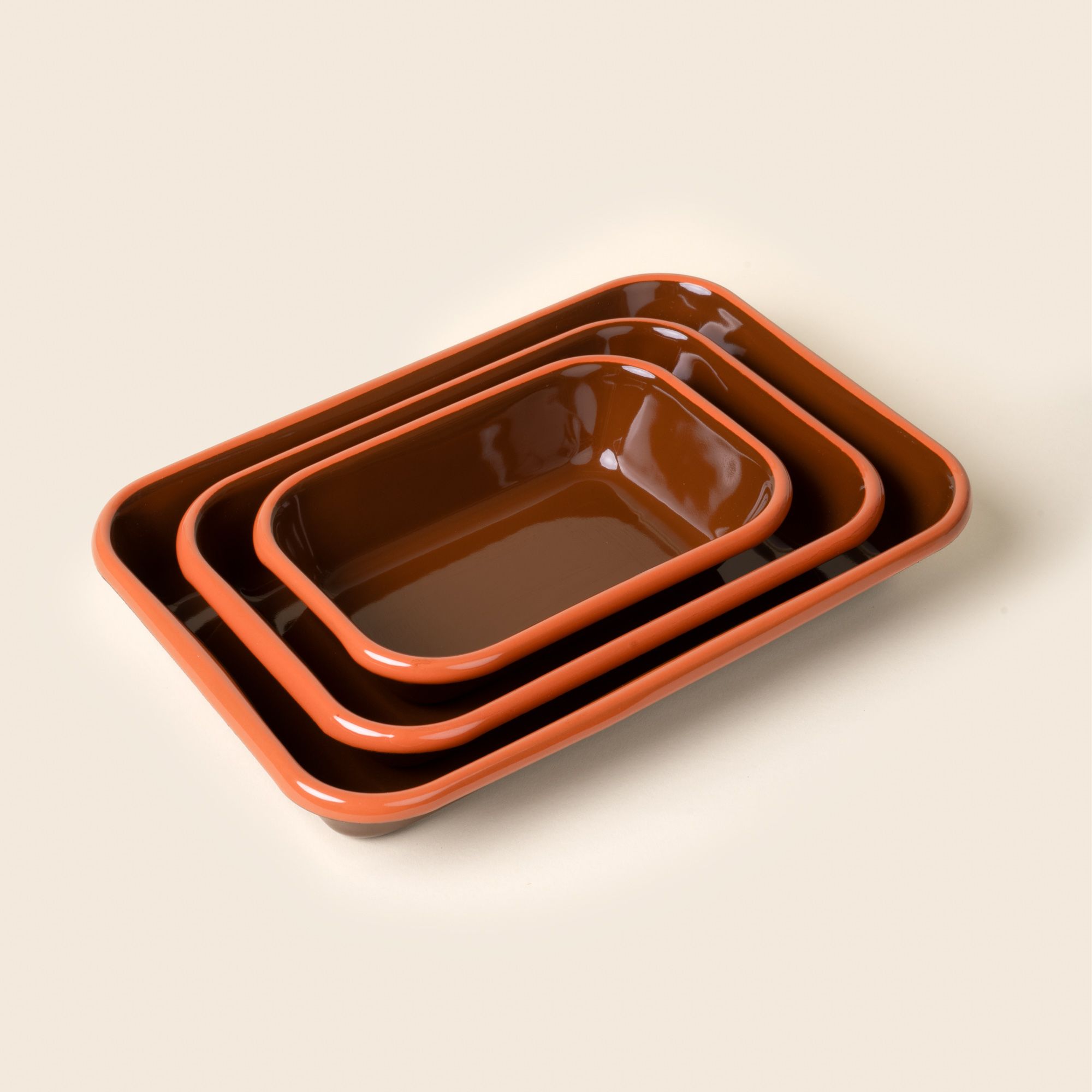 A nesting trio of small, medium, and large rectangular baking dishes in a glossy red-brown color with an orange rim.