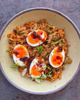 Closeup look of a meal in a ceramic bowl featuring oats, sliced eggs, chili crisp, and light veggies.