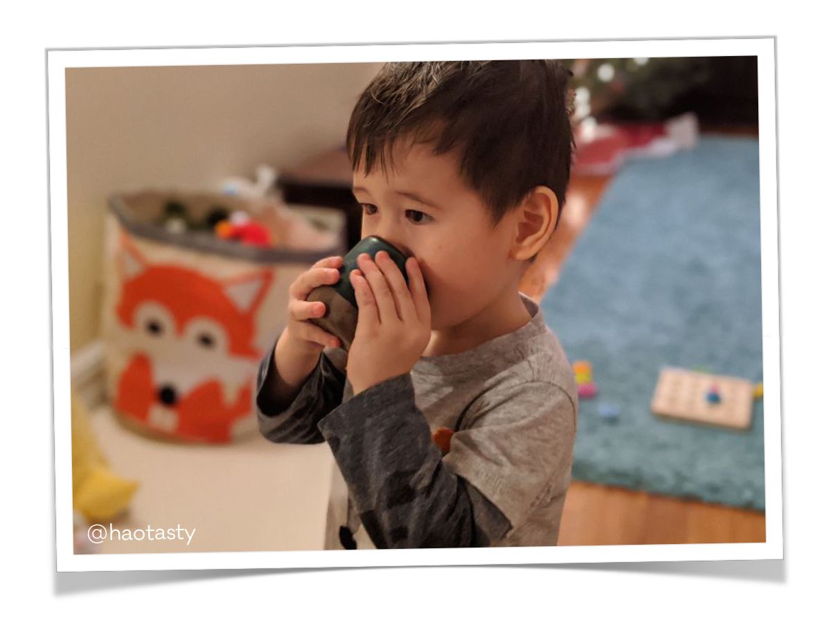 In a playroom, a child holds a ceramic cup to their face.