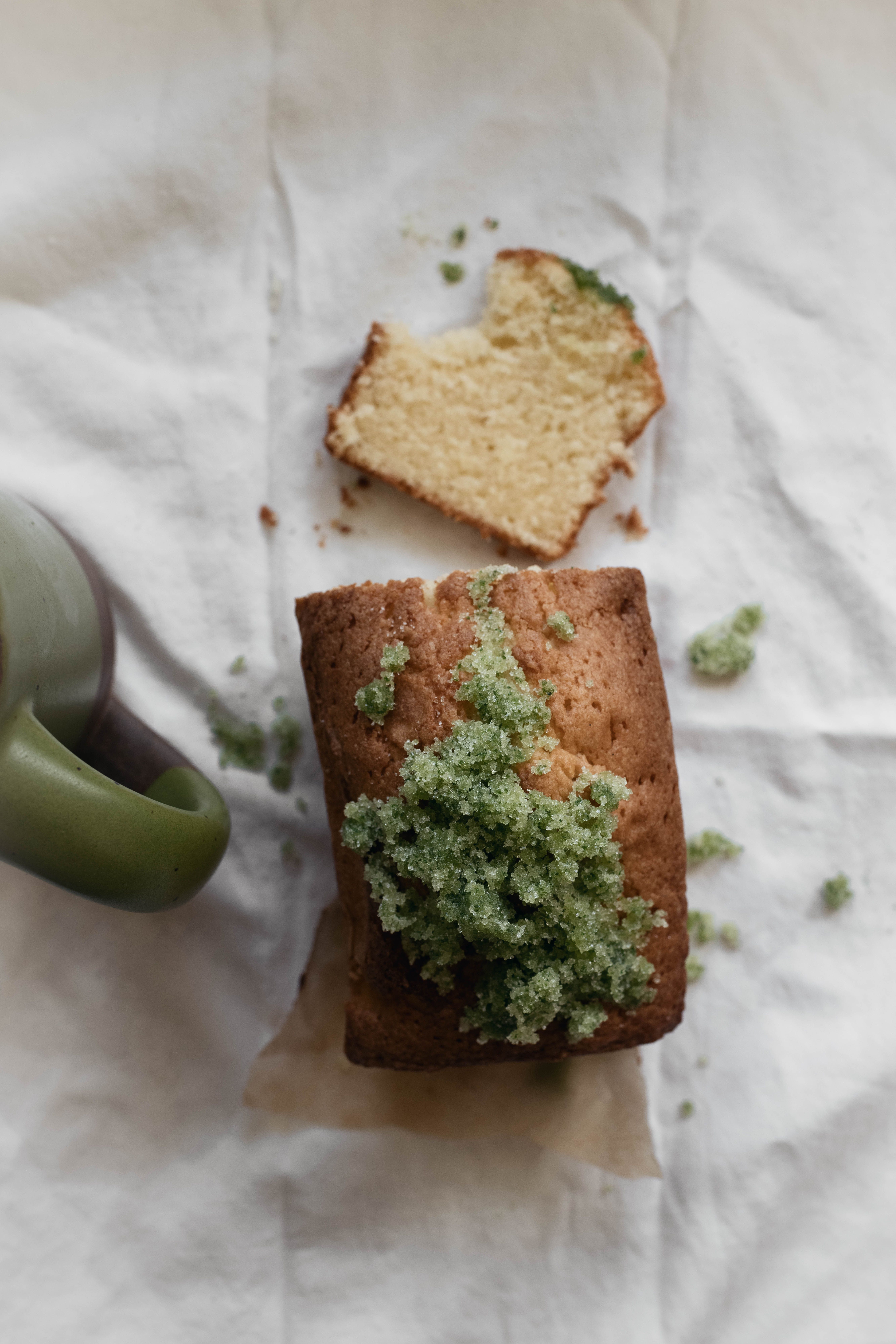 An overhead view of Basil Sugar Pound Cake with 1 slice cut with a bite out of it. A green mug is next to the cake.