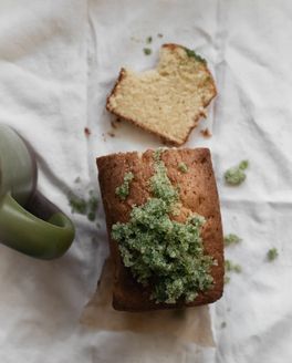An overhead view of Basil Sugar Pound Cake with 1 slice cut with a bite out of it. A green mug is next to the cake.