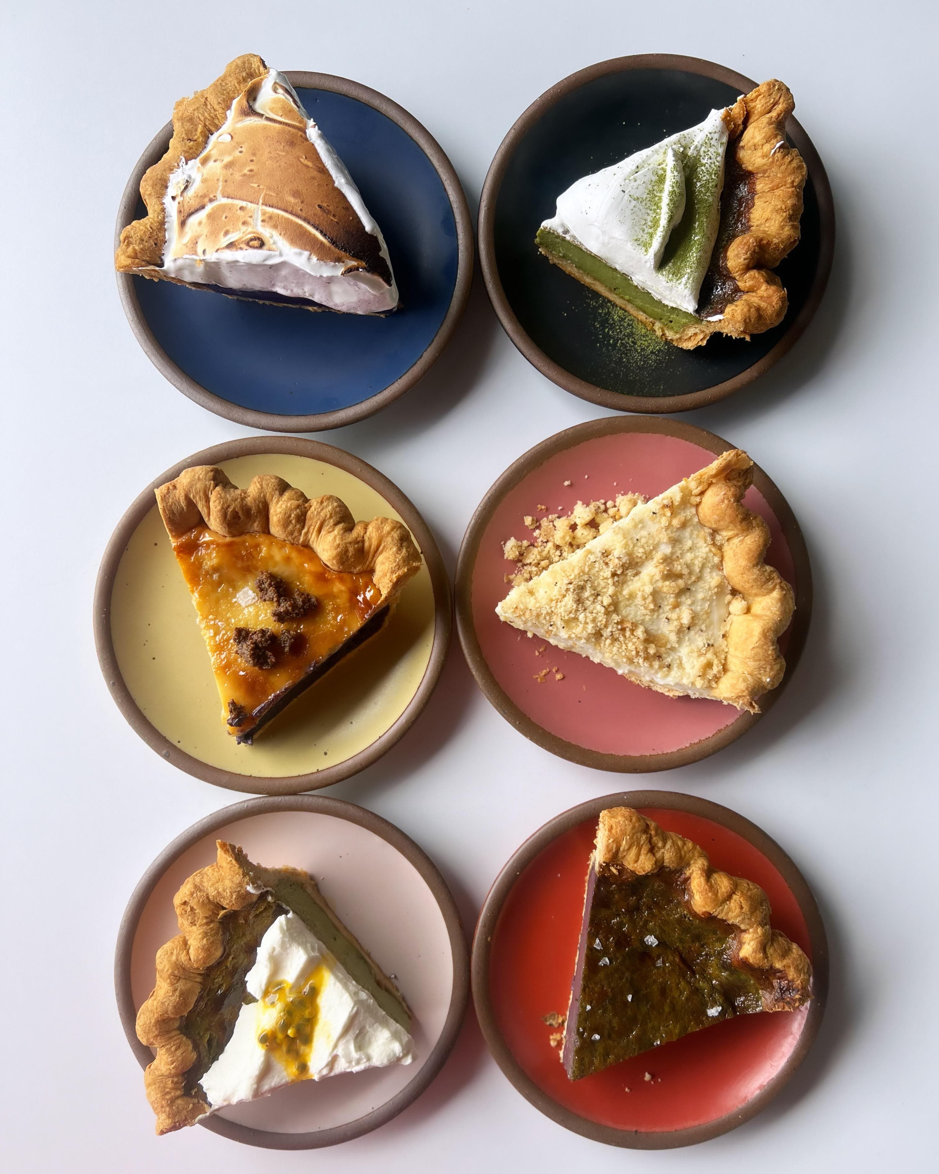 6 colorful plates lined up together, each with a slice of a different pie.