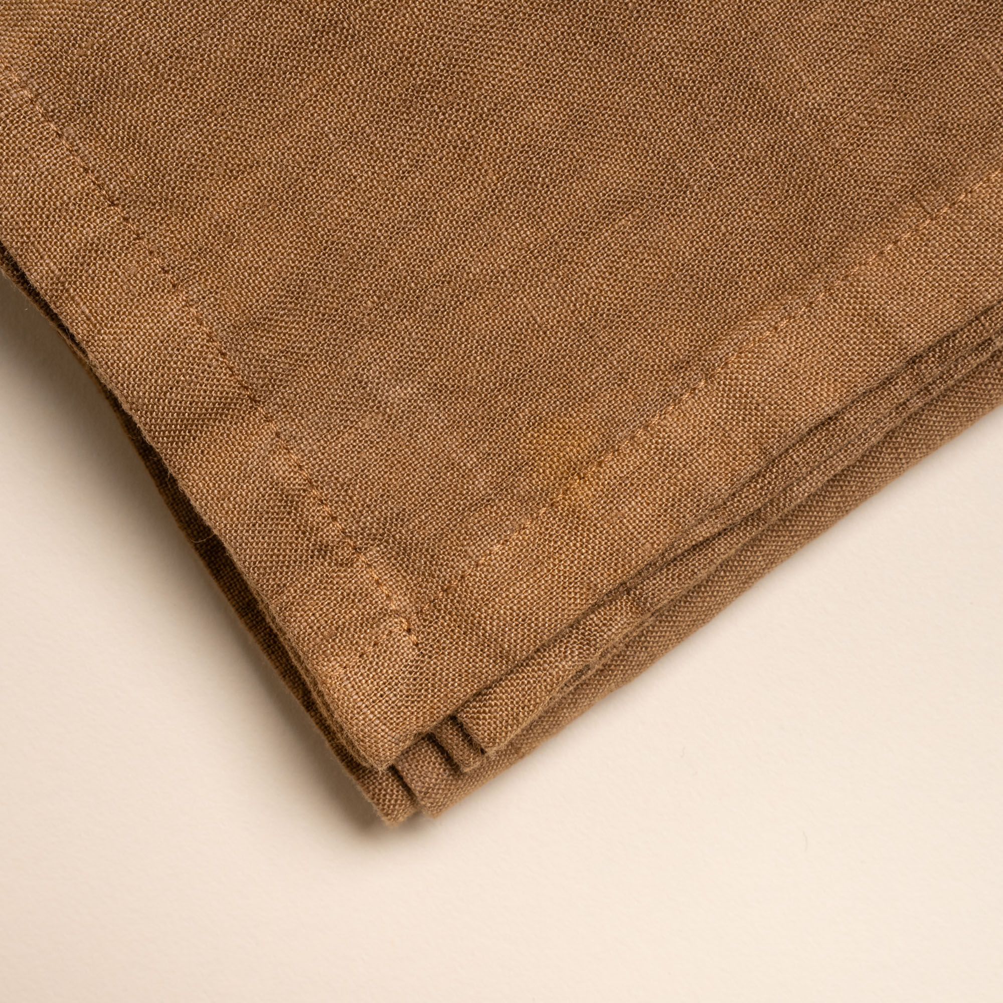 Closeup of the corner of a brown linen napkin on a neutral background.
