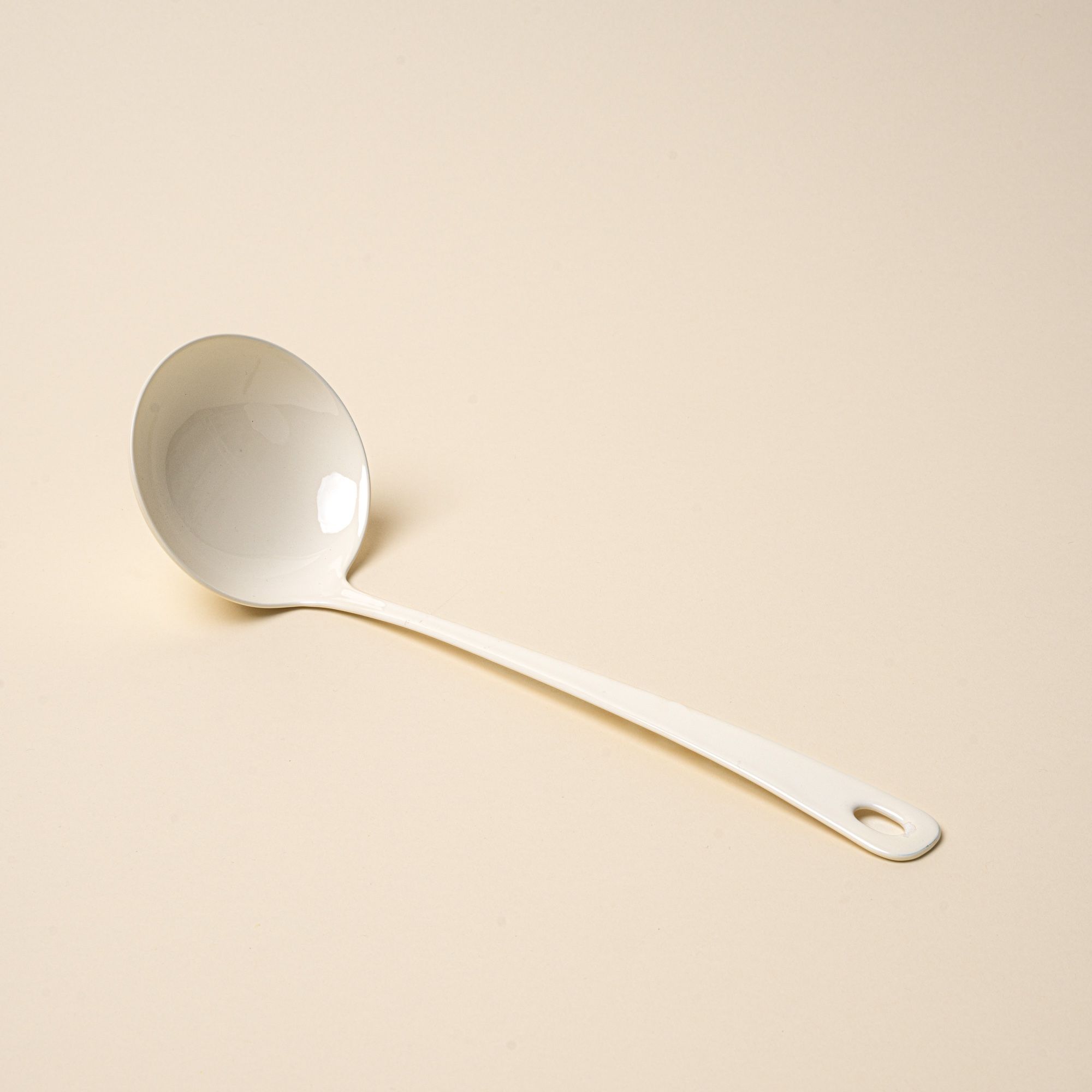 A white enamel ladle with a hole at the end of the handle for hanging.