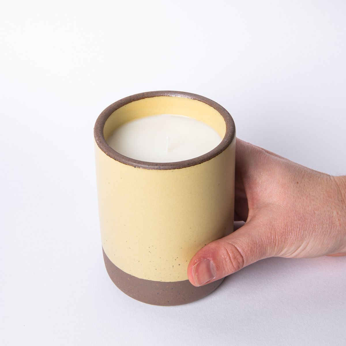 Hand holding a large ceramic vessel in soft butter yellow color with candle inside