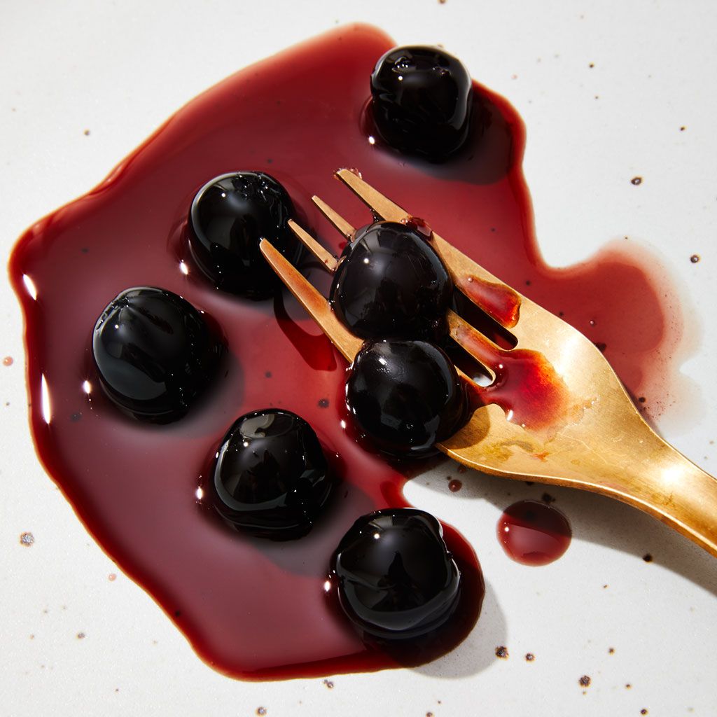 Dark red liquid puddle with six dark red cherries, two held by a brass fork