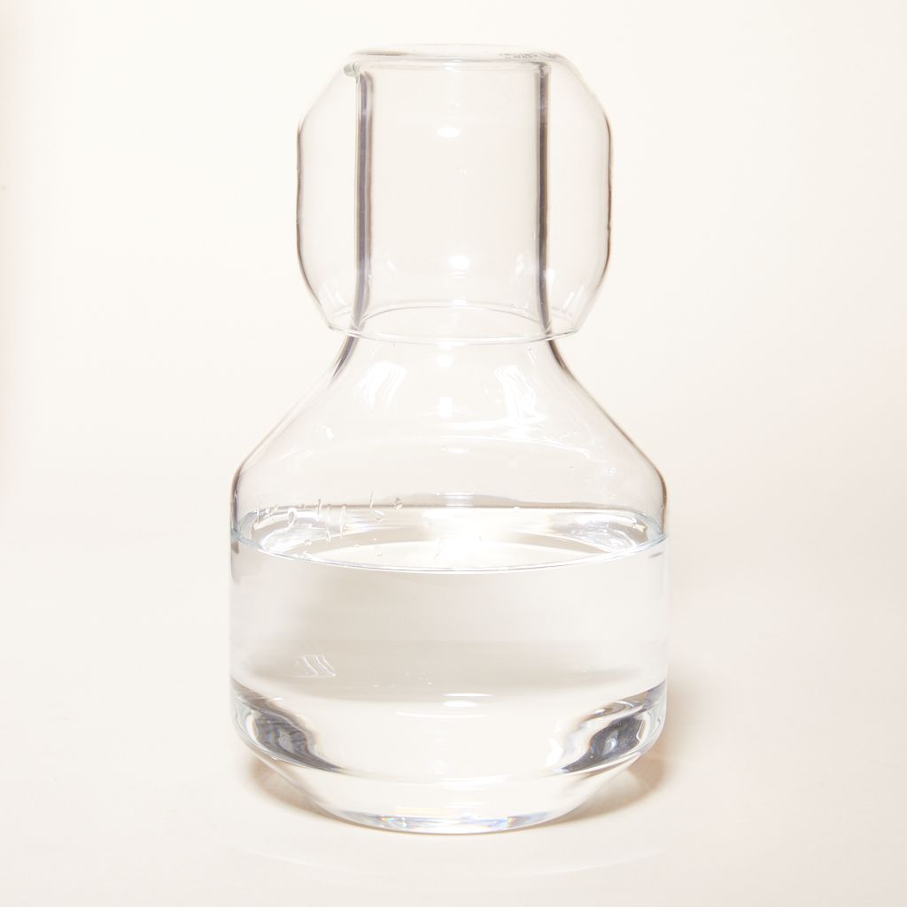 A clear glass carafe with a large base and thinner neck, and a small short water glass fitted on top