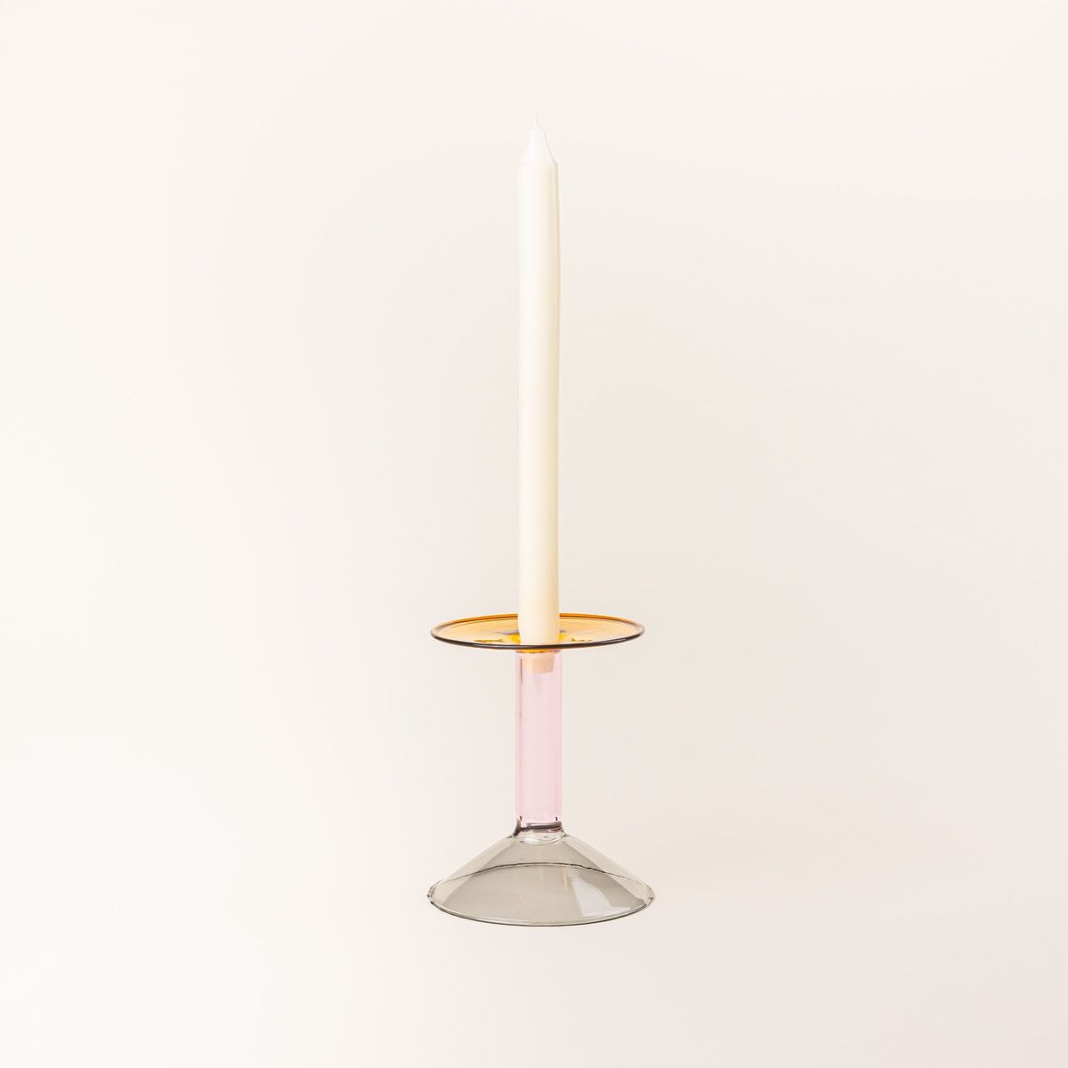 A short modern angular glass candle holder in yellow, pink, and grey colorblocks with a cream taper candle