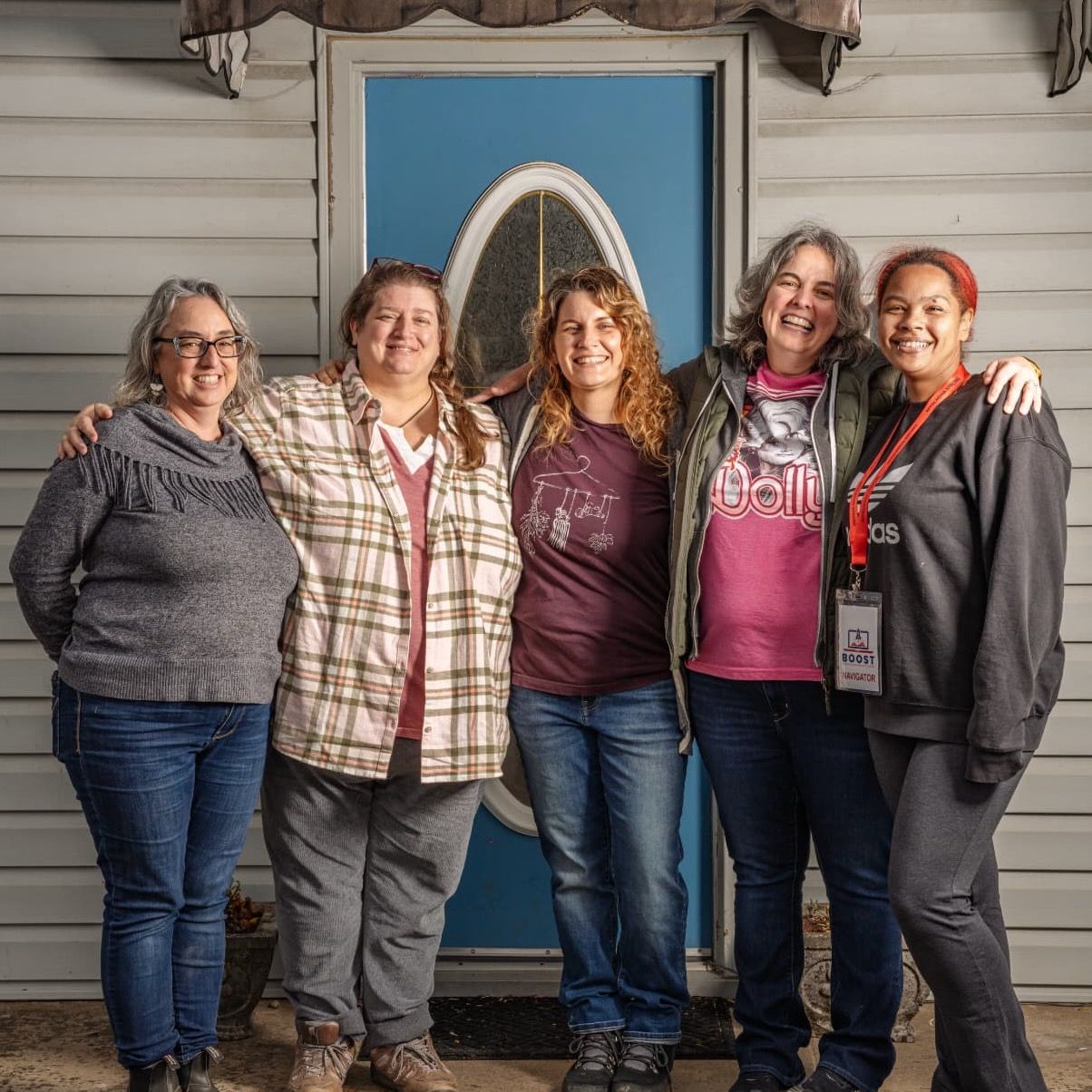 Five people gather together smiling in front of a building with a blue door.