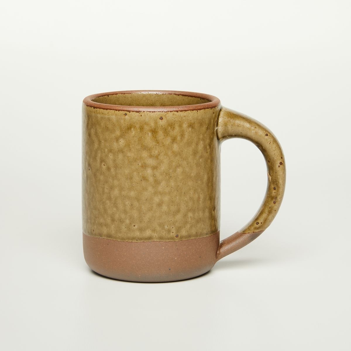A big sized ceramic mug with handle in an earthy green and brown color featuring iron speckles and unglazed rim and bottom base.